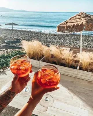 a person holding up two wine glasses in front of the beach at Esperanto seafront studio in Agia Marina Nea Kydonias