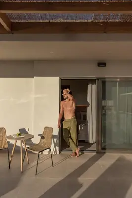 a shirtless man standing on the balcony of a house at Esperanto Seafront suites in Agia Marina Nea Kydonias