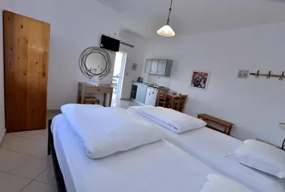 a bedroom with a large white bed and a kitchen at PALEOCHORA FINIKAS Apartments in Palaiochóra