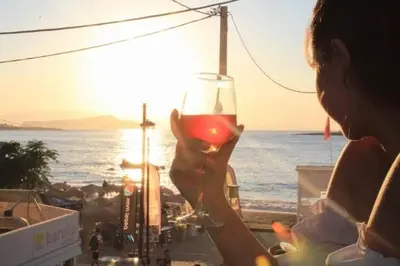 a woman holding a glass of wine at the beach at Rika’s seaside apartments in Chania Town