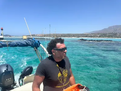 a man sitting on a boat in the water at Beautiful Life Rooms with Sea View - Next to Elafonisi Beach in Elafonisi