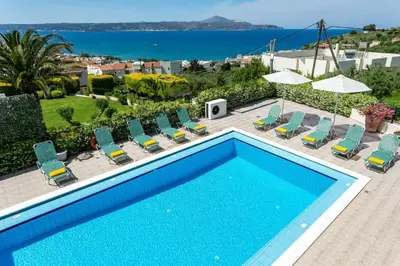 a swimming pool with chairs and umbrellas and the ocean at Villa Katerina Pente by Villa Plus in Kalyves