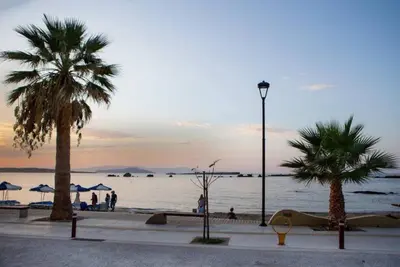 a beach with palm trees and the ocean at sunset at Christina_Apt in Chania Town