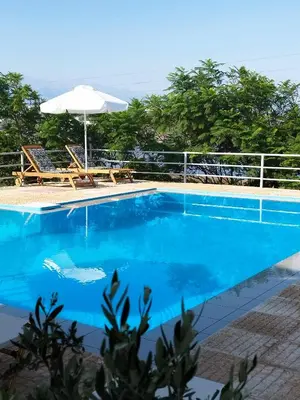 a blue swimming pool with an umbrella and chairs at Nostalgia Villas in Tersanas