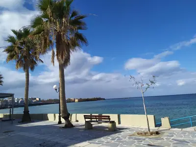 a bench on the beach with palm trees and the ocean at Rubini City Apartment in Chania Town