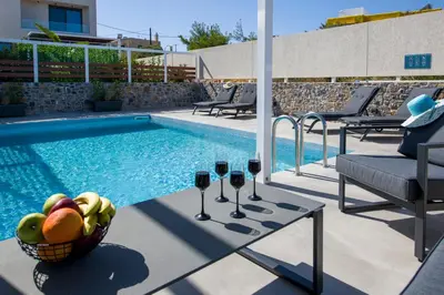 a pool with two glasses of wine and a basket of fruit at Xenias Luxury Villas Kalathas in Kalathas