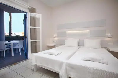 a white bedroom with a large bed and a table at Studios Vasilis in Agia Marina Nea Kydonias