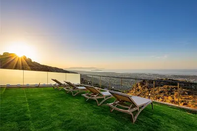 a row of lounge chairs on a balcony with the sunset at Villa Mari Chania, with private ecologic pool and amazing view! in Chania Town