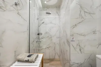 a bathroom with a shower with white marble walls at Luxury Pearl, steps to the beach in Chania Town