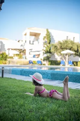 a little girl laying on the grass near a swimming pool at Villa Rodo in Pírgos Psilonérou