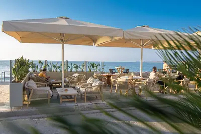 people sitting at tables under an umbrella on the beach at PLUS 2! in Chania Town