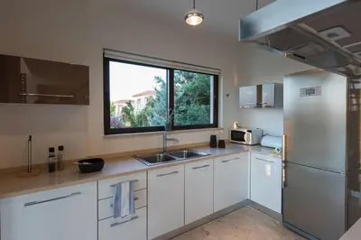 a kitchen with white cabinets and a sink and a window at Magnifique villa avec piscine au bord de mer in Chorafakia