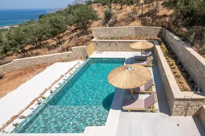 a swimming pool with chairs and umbrellas and the ocean at Alma Natura Villas Falasarna- Avgerinos Villa in Falasarna
