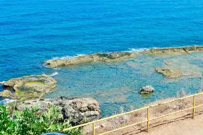 a beach with blue water and rocks and a fence at Elpida Seafront Paradise apartment in Crete in Chania Town