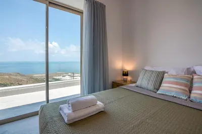 a bedroom with a large window with a view of the ocean at Alma Natura Villas Falasarna - Aposperitis Villa in Falasarna