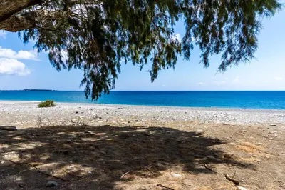a view of the beach from under a tree at Akra Grammeno Beachfront Villas in Palaiochóra