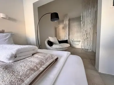 a bedroom with a bed with white sheets and a chair at Perla Coco Jacuzzi Suites in Chania Town