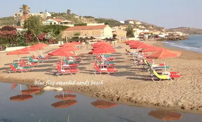 a beach with chairs and umbrellas and the water at Asterias Studios & Apartments in Kalyves