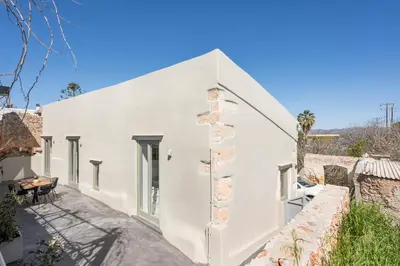 a white house with a stone wall at Tholos Cottage in Stérnai