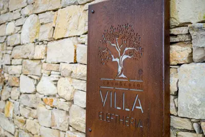 a sign for a villa with a tree on a stone wall at Brand new Villa Eleftheria BY APOKORONAS-VILLAS in Plaka