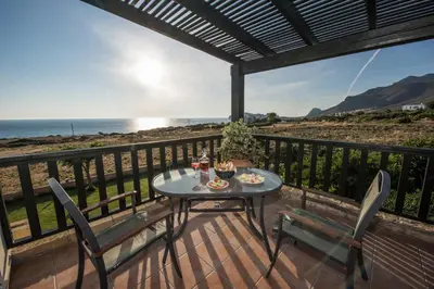a table and chairs on a deck with a view of the ocean at Magnolia Apartments and Studios in Falasarna