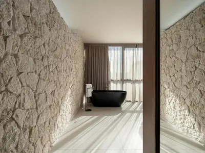 a bathroom with a stone wall and a black tub at Pnoe Villas - Seafront Experience in Tavronitis
