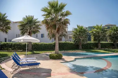 a pool with a chair and an umbrella and palm trees at Calmaliving Seaside apartments with pool in Gerani Chanion