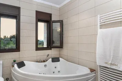 a white tub in a bathroom with two windows at Heliopetra Lux Villa with private Pool in Varípetron