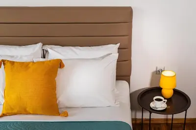 a bed with white pillows and a yellow lamp on a table at Central apt. with parking - 3 min from old port in Chania Town