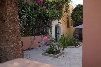 a little girl is sitting in a garden next to a building at Lindas Convent Garden Home 2 in Chania Town