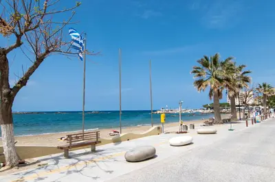 a beach with benches and palm trees and the ocean at Michail Suite Chania δίπλα στην παραλία της πόλης in Chania Town